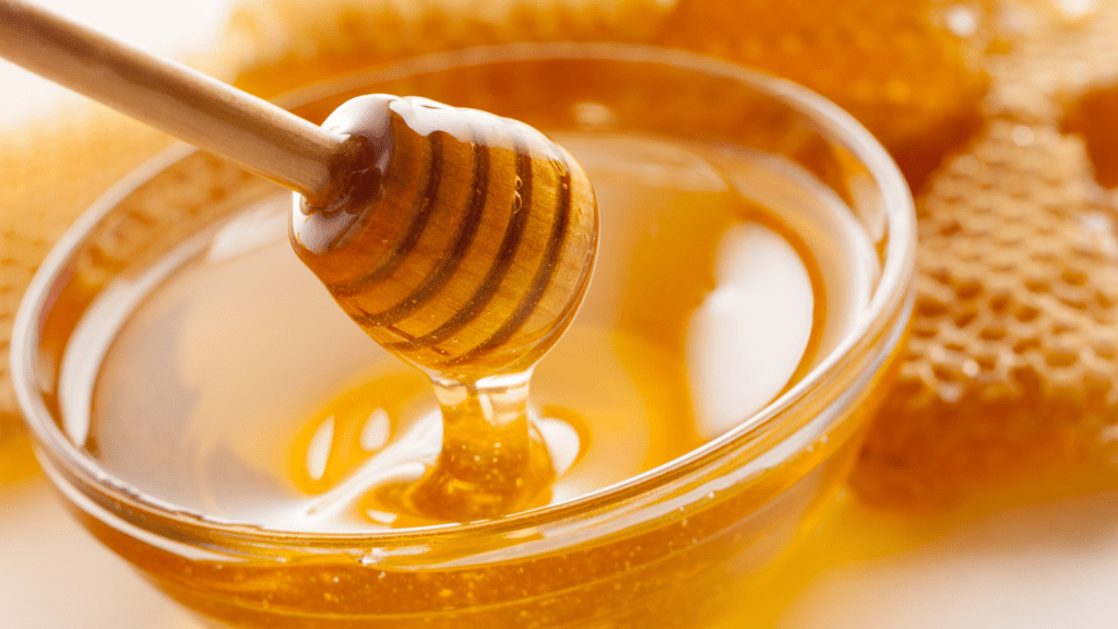 A jar of honey with honeycomb and a wooden honey dipper.