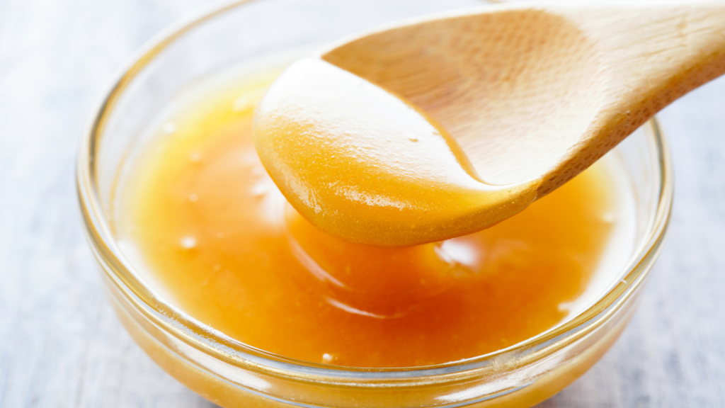 "A jar of golden Manuka honey with a wooden honey dipper, emphasizing its rich texture and medicinal properties, sourced from the Manuka bush in New Zealand